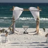 Beach wedding arch with white drapes facing the ocean and waves