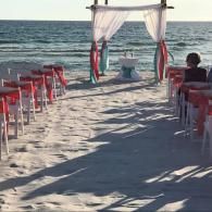 Beach wedding aisle with white drapes, red chairs, and an ocean view