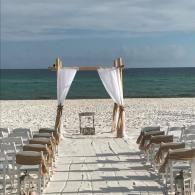 Beach wedding setup with white chairs and a draped arch facing the ocean