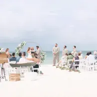 Outdoor beach wedding ceremony with white chairs, floral arch, and guests facing the ocean