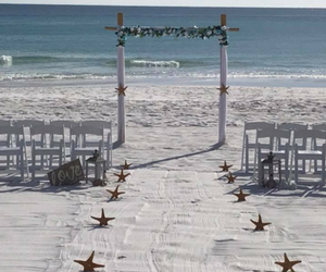 Beach wedding setup with white chairs, starfish aisle, and floral arch facing the ocean