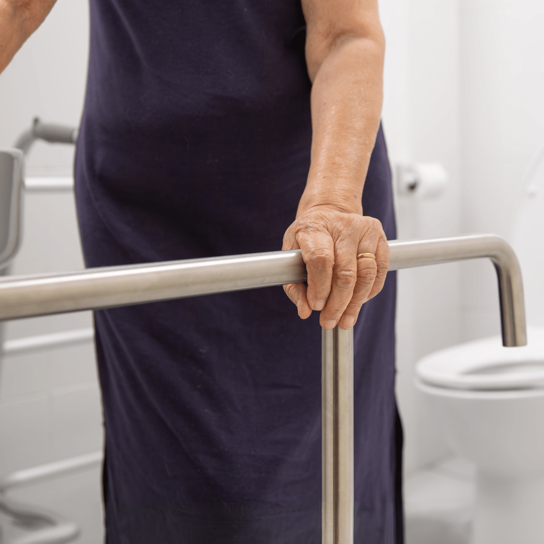 An elderly woman is holding onto a railing in a bathroom