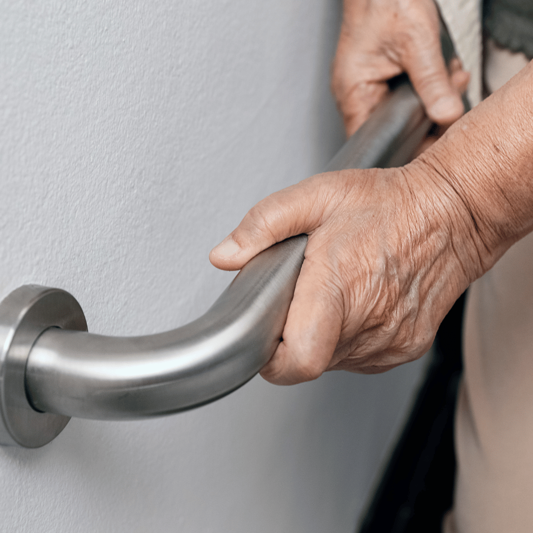 An elderly woman is holding a stainless steel handle in a bathroom.