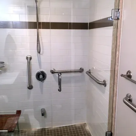 A bathroom with a walk in shower with a glass door and stainless steel handles.