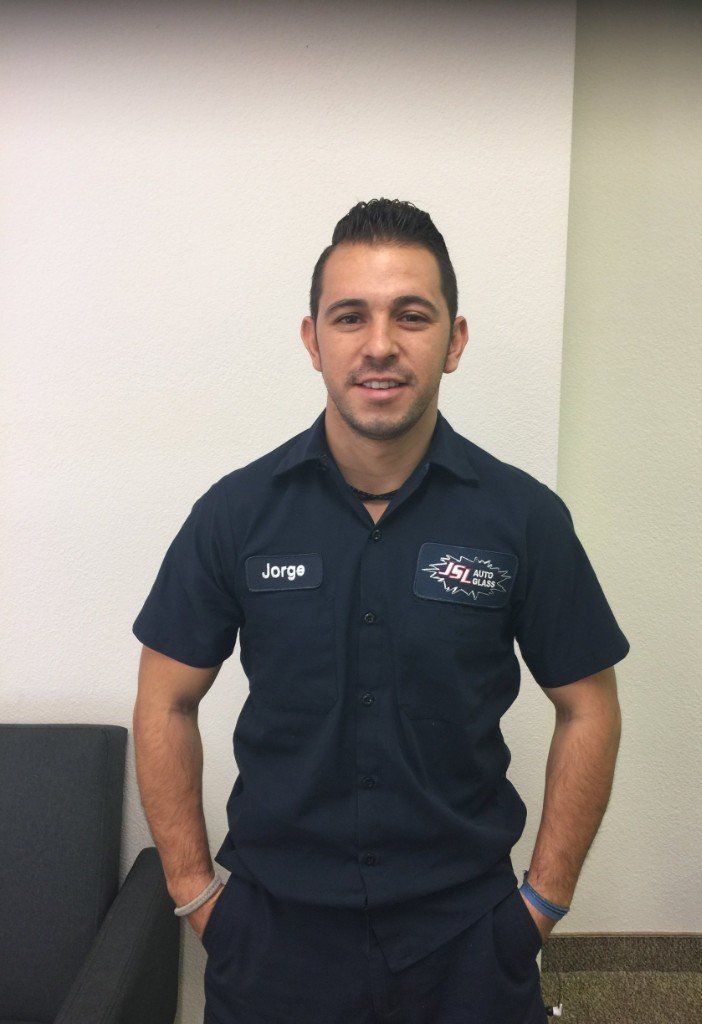 A woman wearing glasses and a necklace is smiling while sitting in a car.
