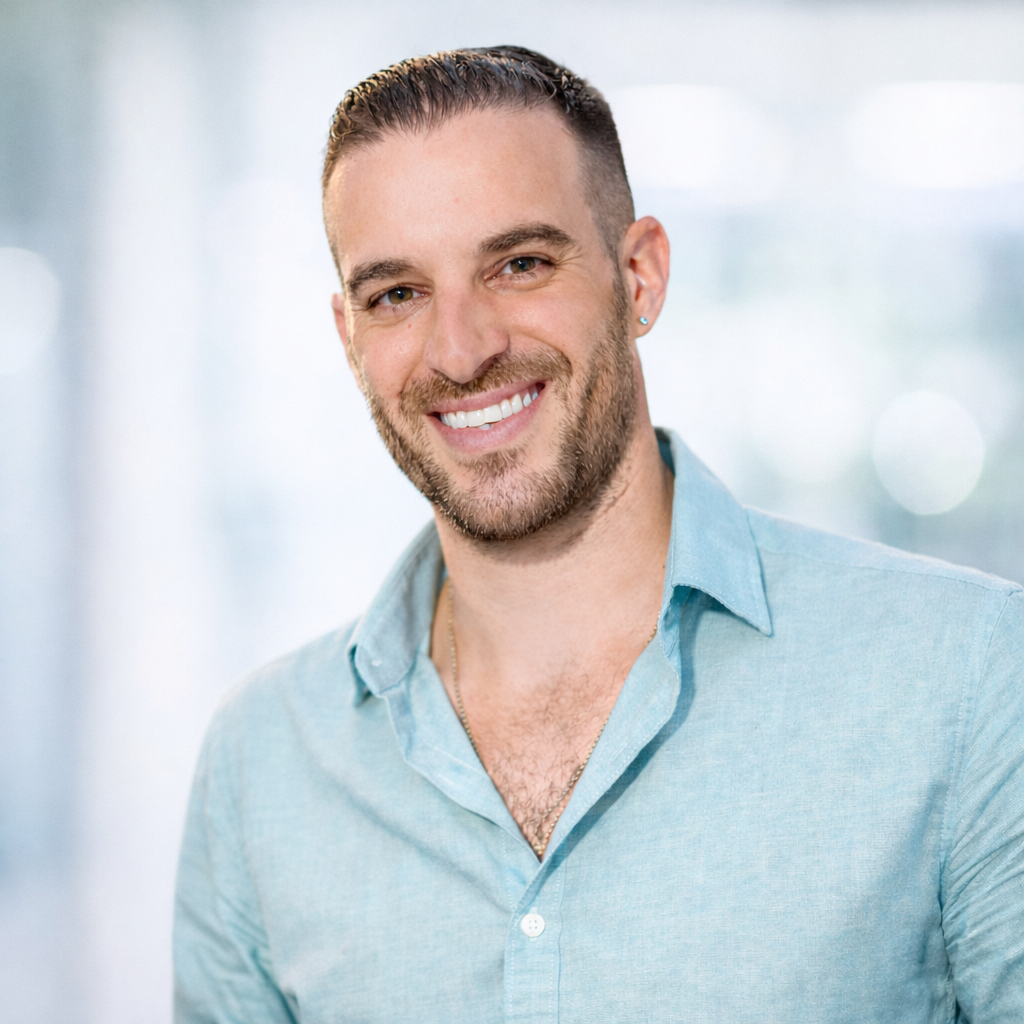 Smiling man in light-colored shirt, looking at the camera. Black and white, blurred background.