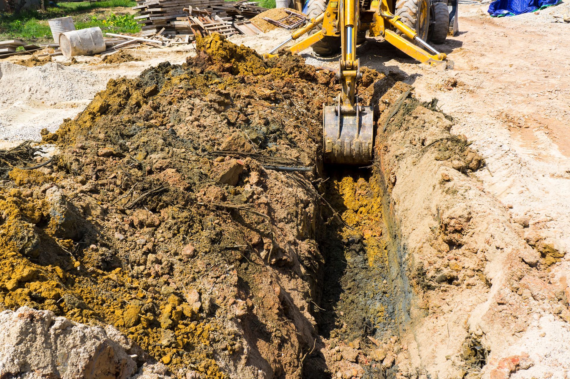 A yellow excavator is digging a trench in the dirt.