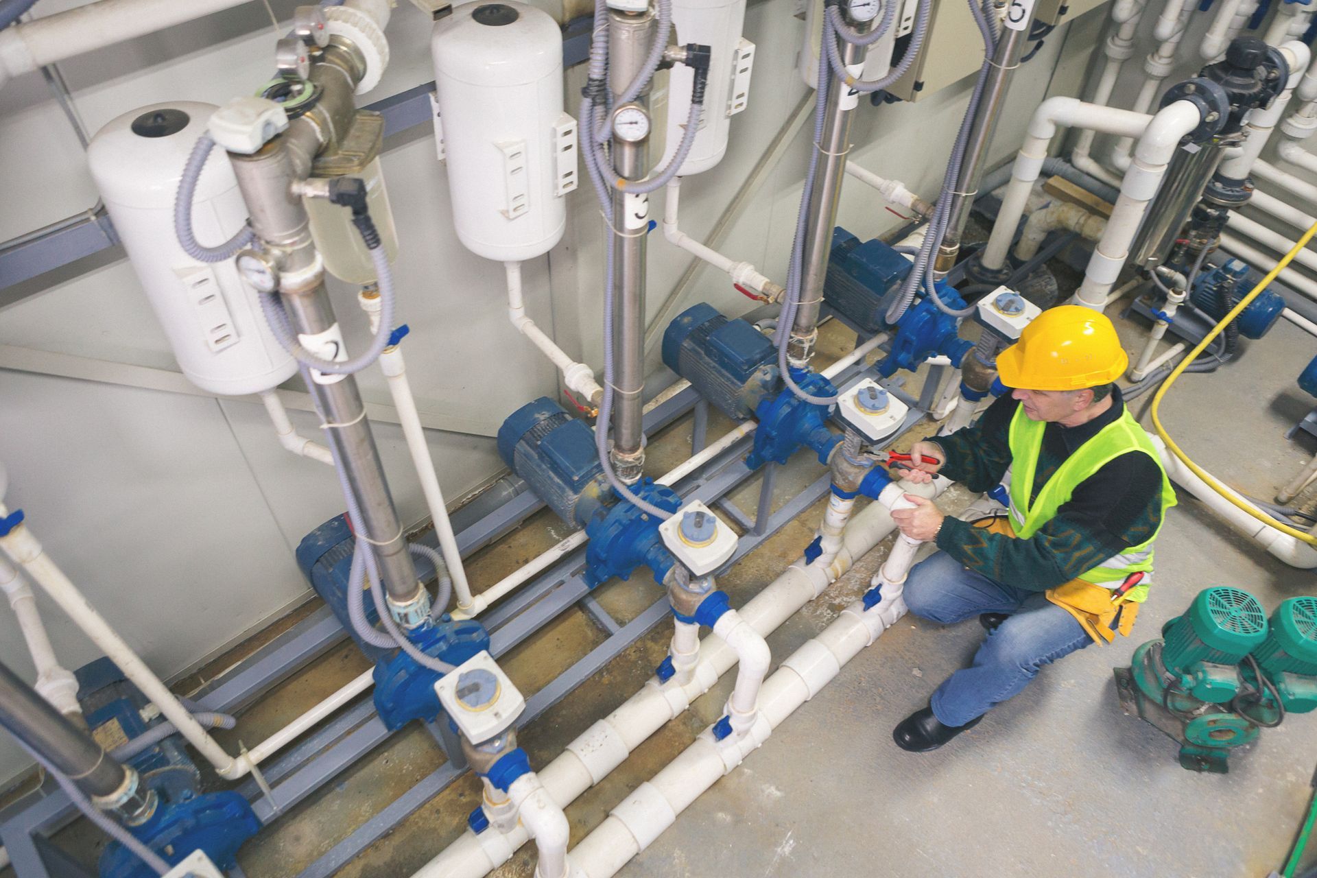A male commercial plumber checks on the pipes of a boiler room.