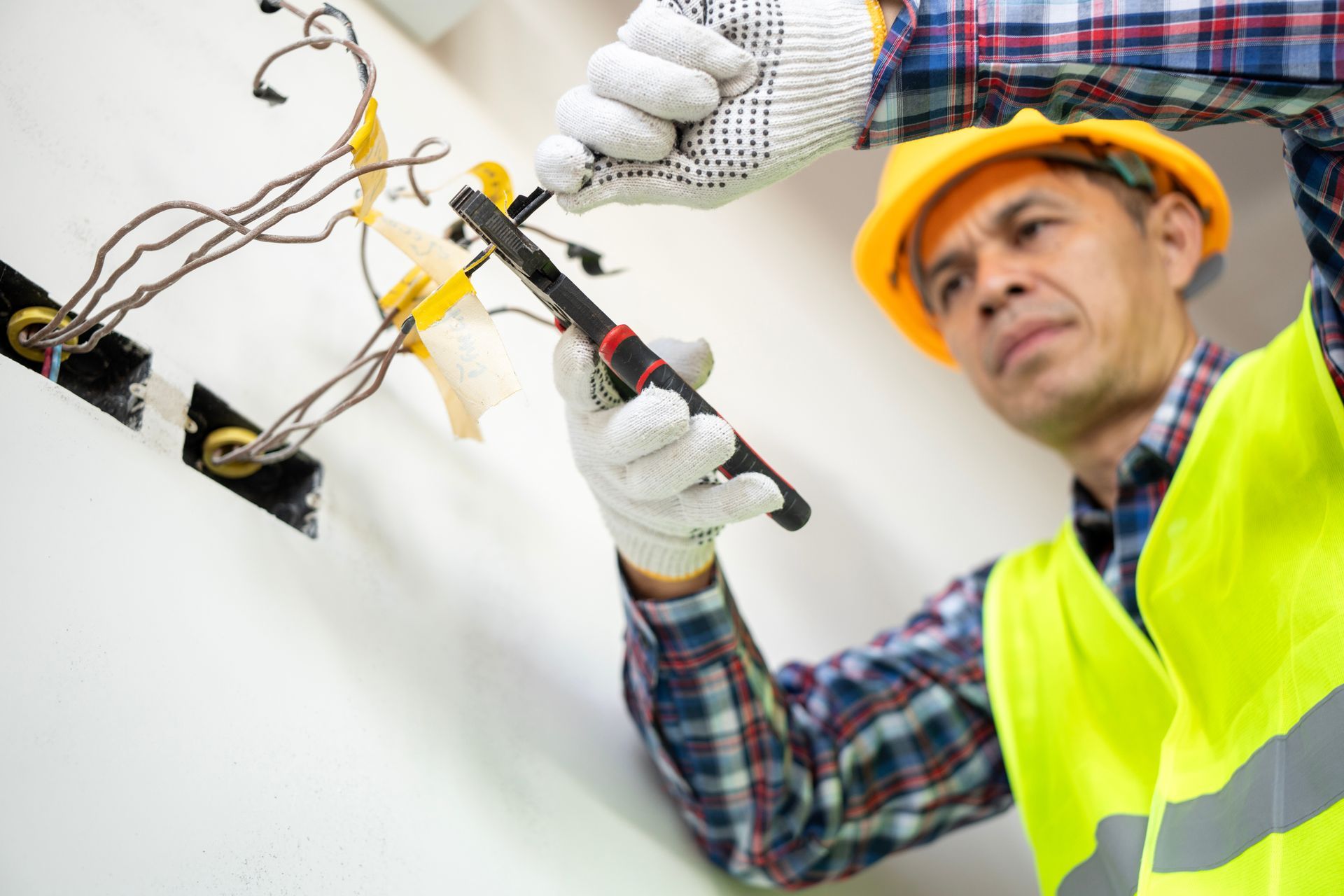 An electrician working on exposed wall wiring using insulated tools and gloves