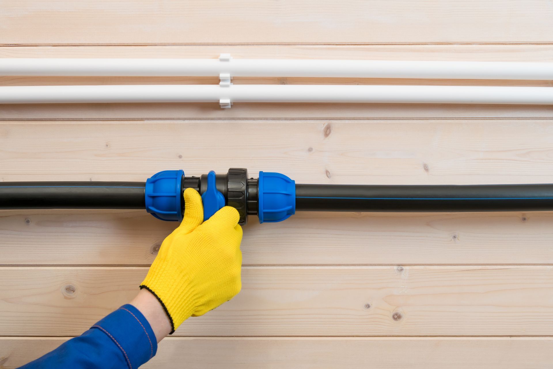 A gloved hand closes a water supply pipe on a wall.