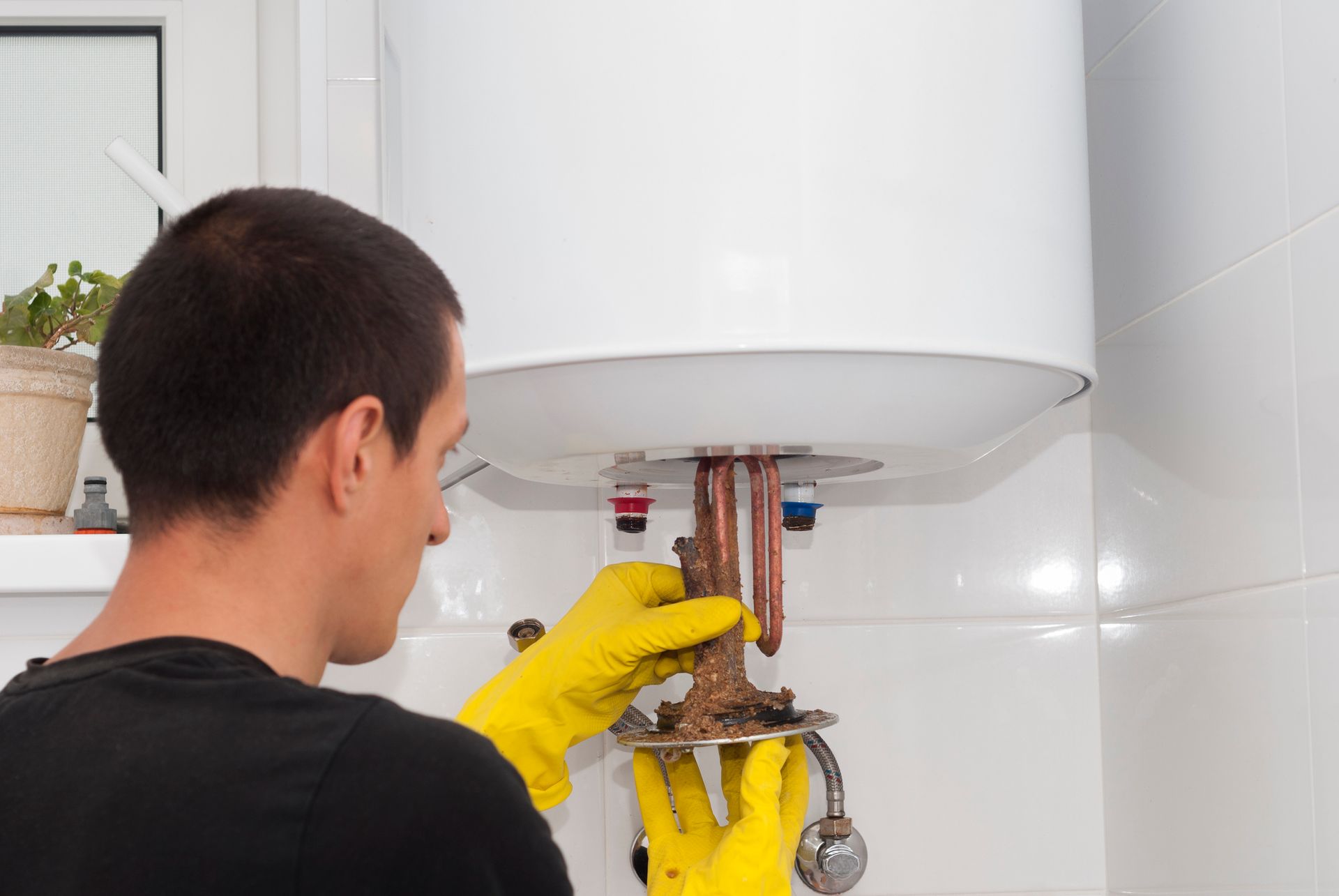 Male plumber checks on the corrosion of a white and working broiler.