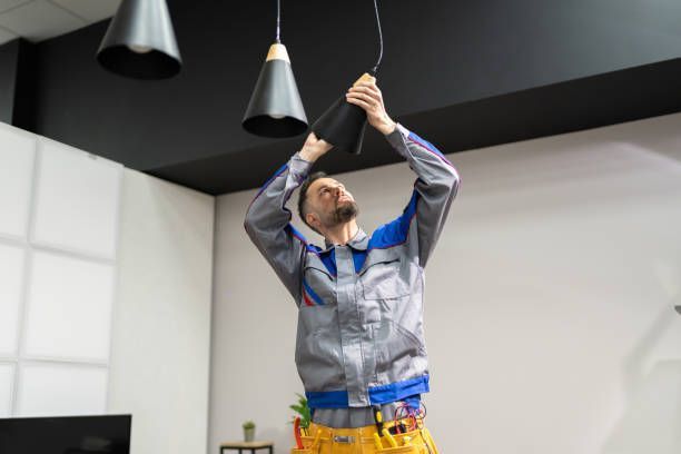 Electrician checking ceiling light fixture, highlighting quality electric services at home.
