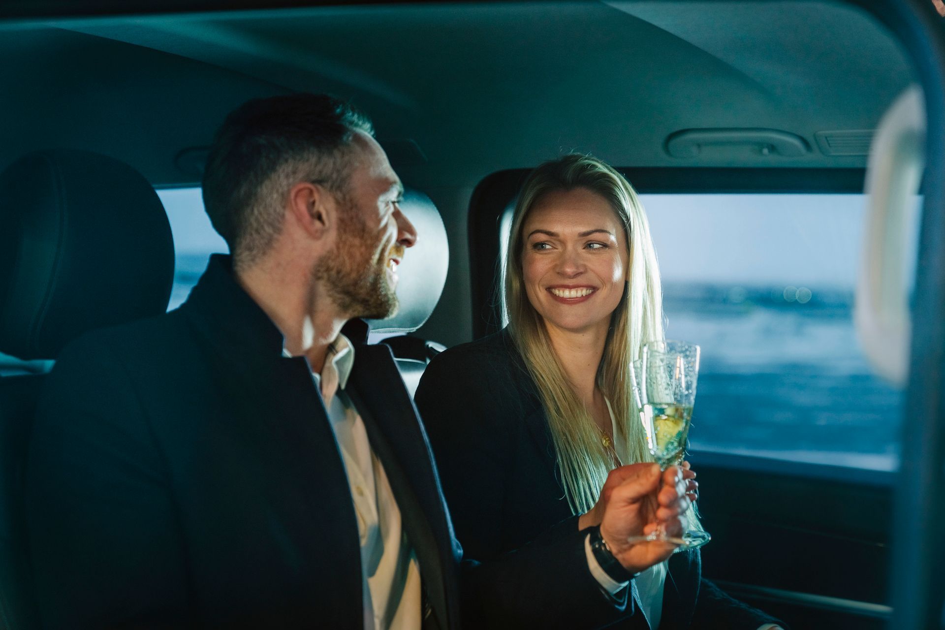 A man and a woman are sitting in the back seat of a car holding wine glasses. A man and a woman are sitting in the back seat of a car holding wine glasses.