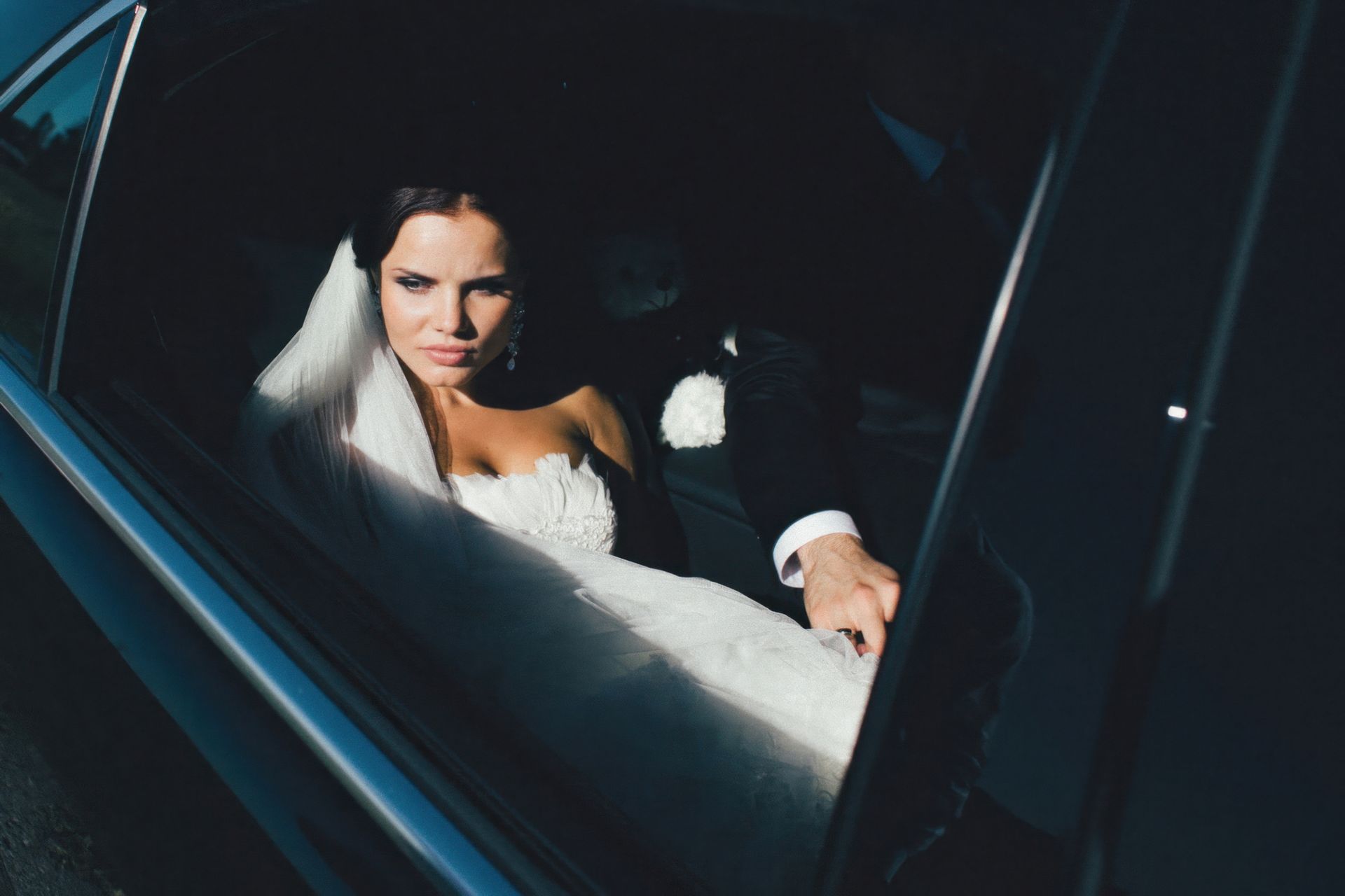 A bride and groom are sitting in a car looking out the window. A bride and groom are sitting in a car looking out the window.