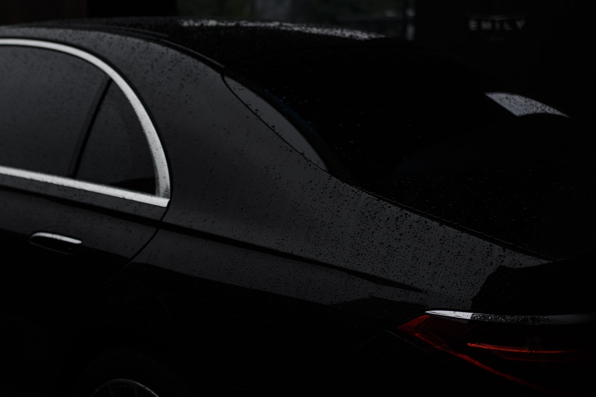 A black car is parked in the rain in the dark.