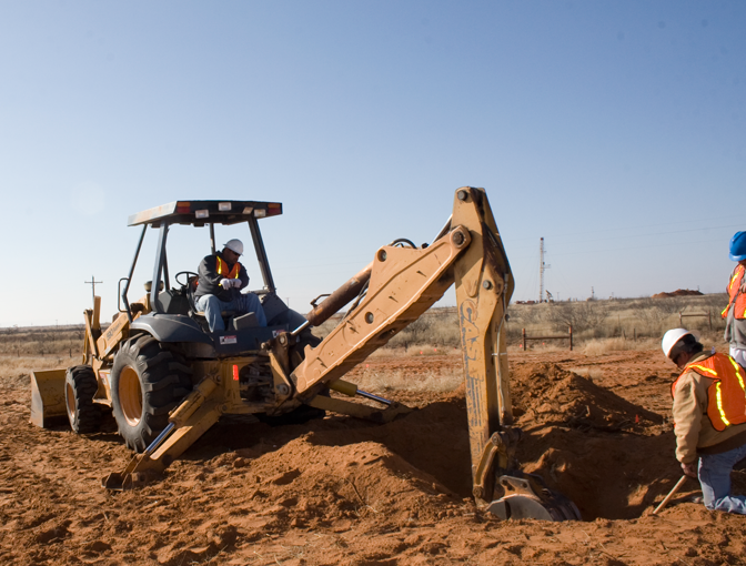 Two construction workers are digging a hole with a backhoe