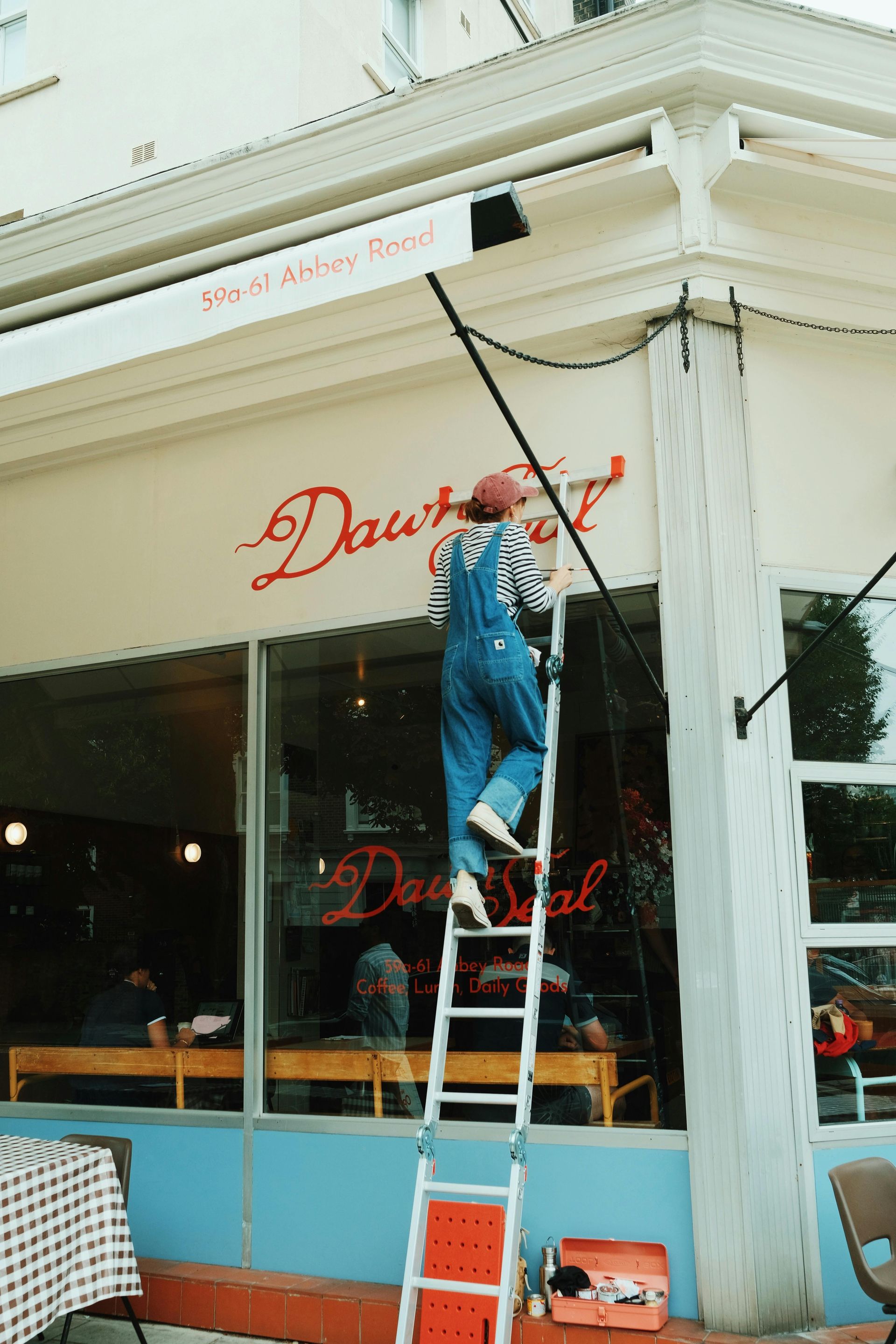 Person on a ladder working on a storefront sign that reads 