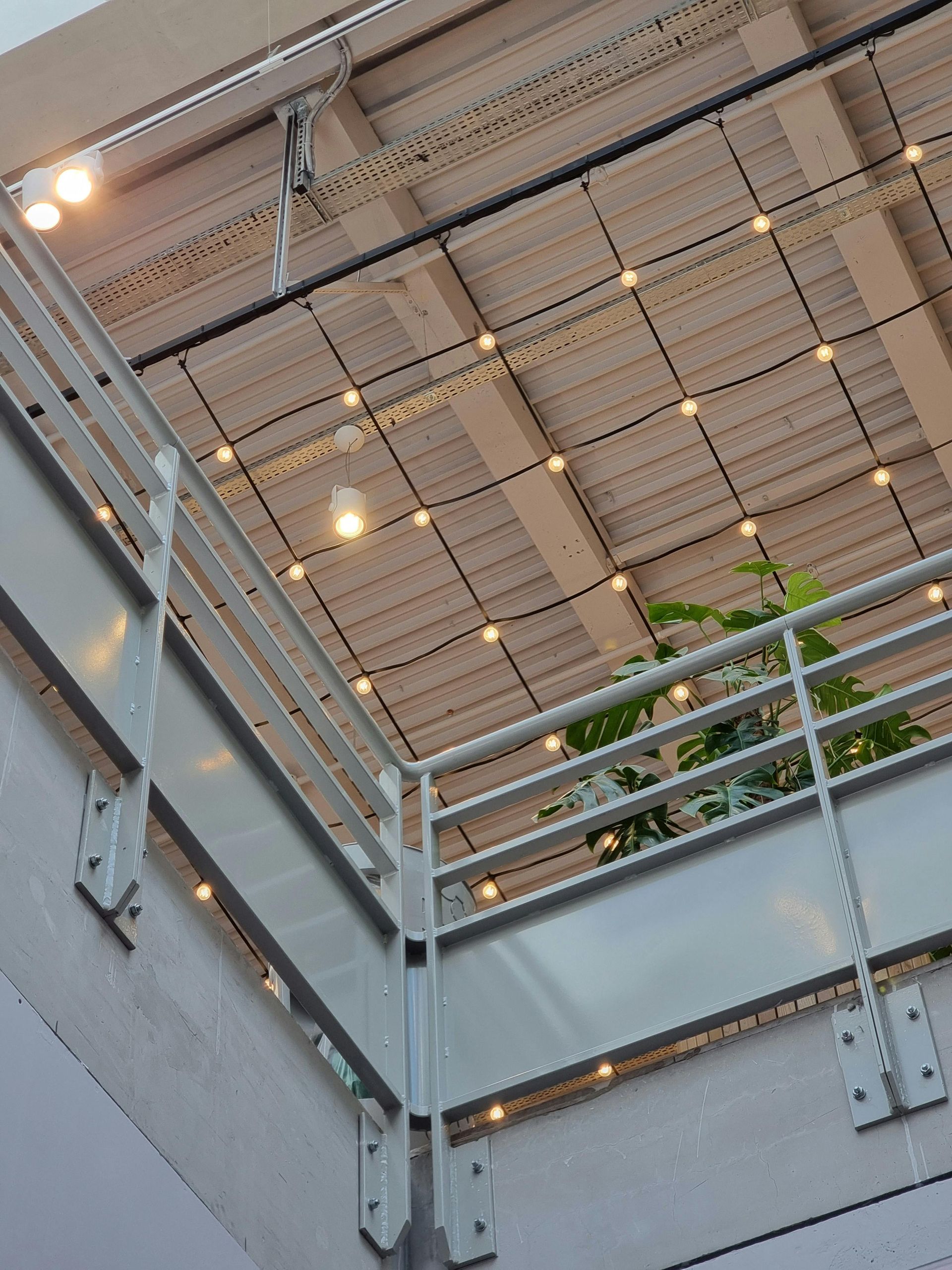 Indoor balcony with metal railing, string lights, and a potted plant.