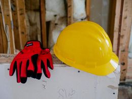 Yellow hard hat and red work gloves on drywall in a construction setting.