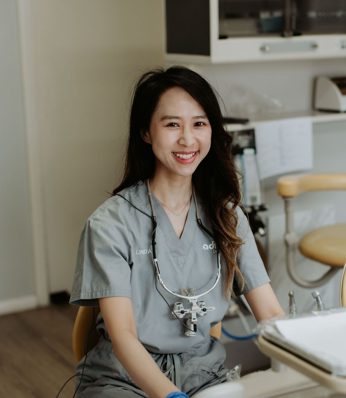 A female dentist is sitting at a desk in a dental office.