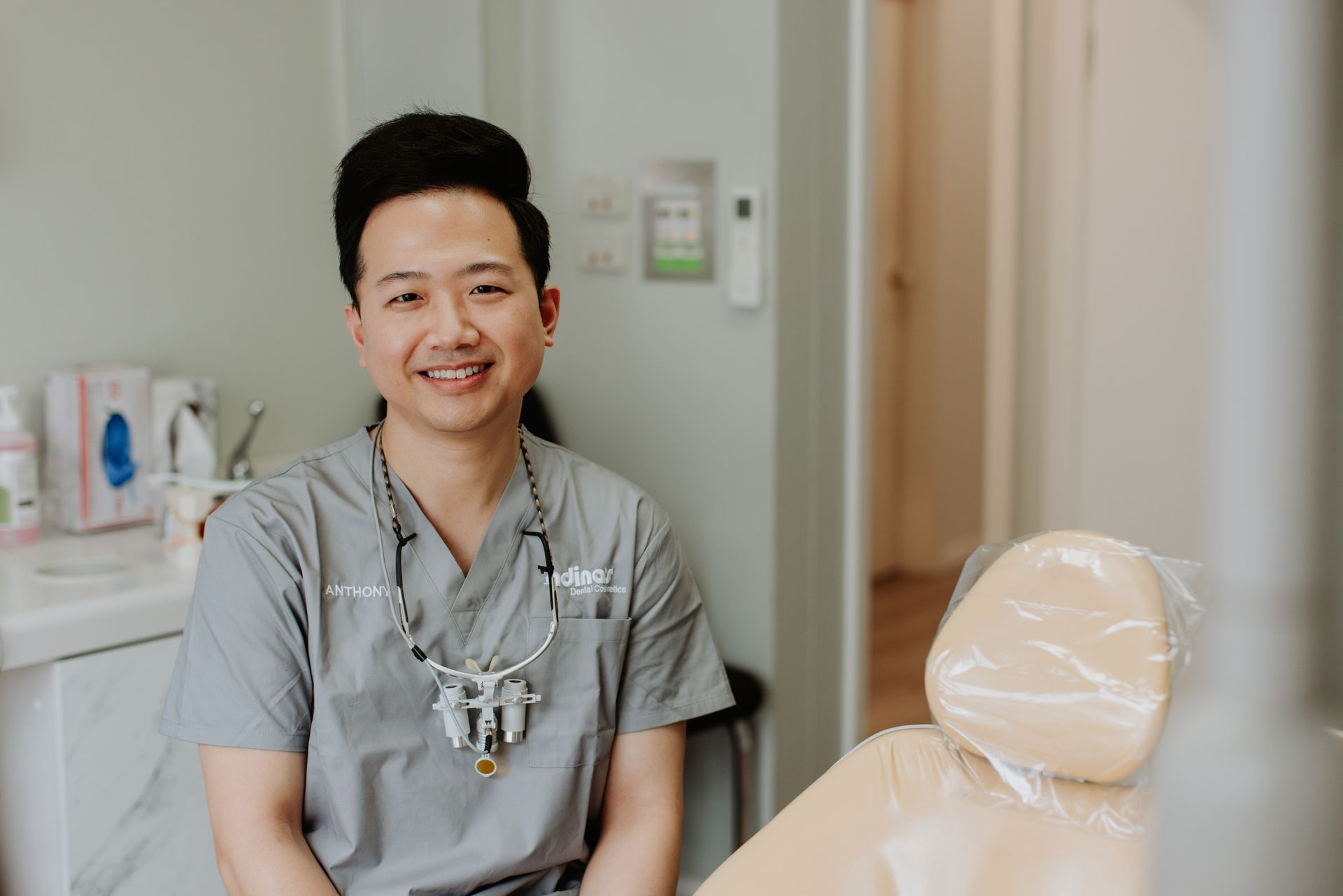 A dentist is sitting in a dental chair and smiling at the camera.
