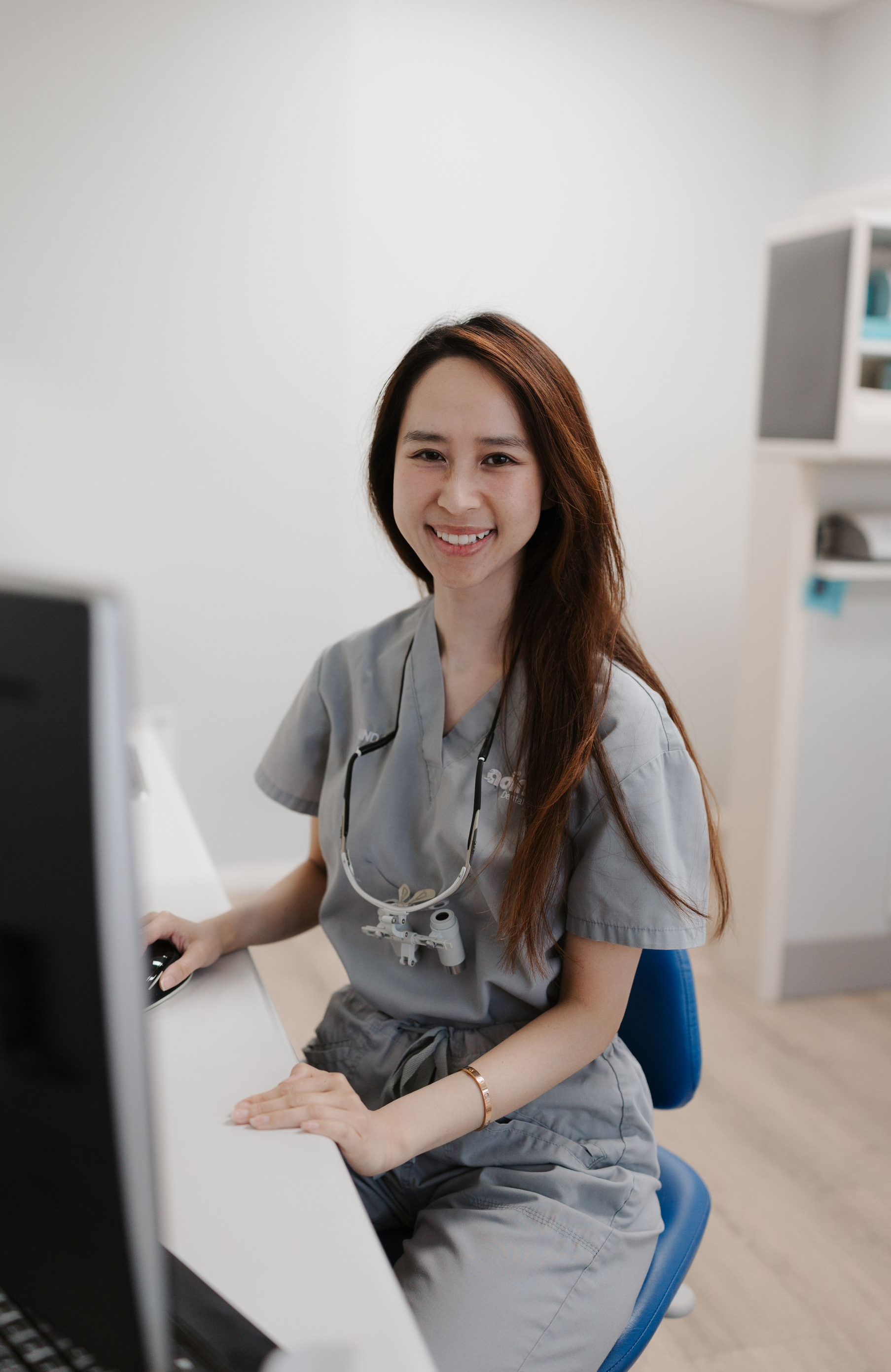A female dentist is sitting at a desk in a dental office.
