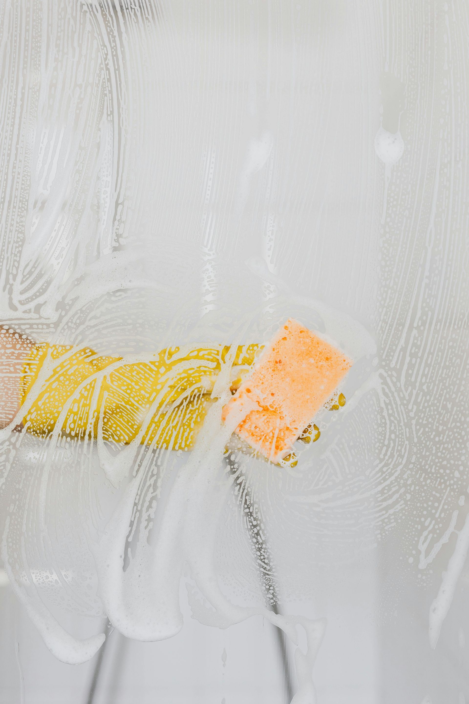 A person is cleaning a shower door with a sponge.