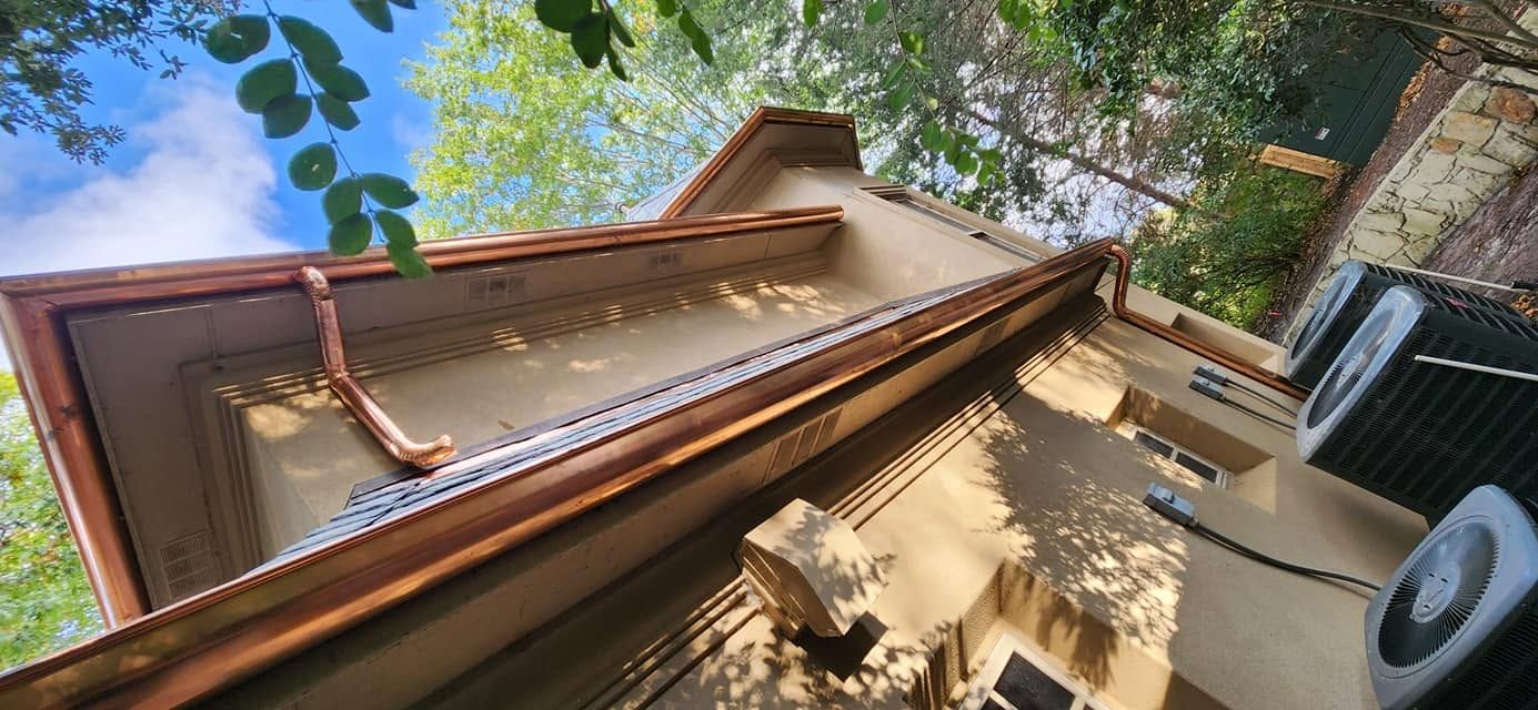Upward view of a tall wooden ladder against a house wall, with trees and blue sky overhead