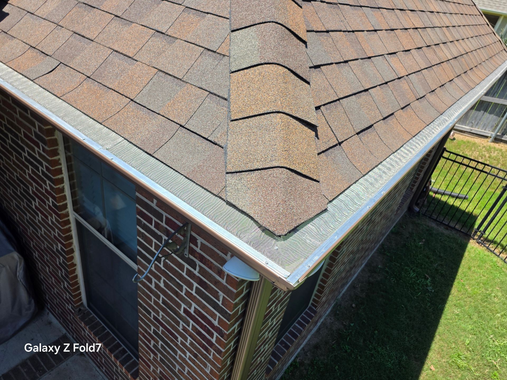 Roof and brick exterior corner of a house with shingled gable roof and small window