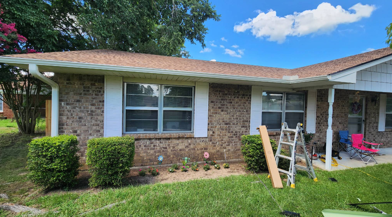 Single-story brick house with white shutters, lawn, and a ladder and tools by the front porch.