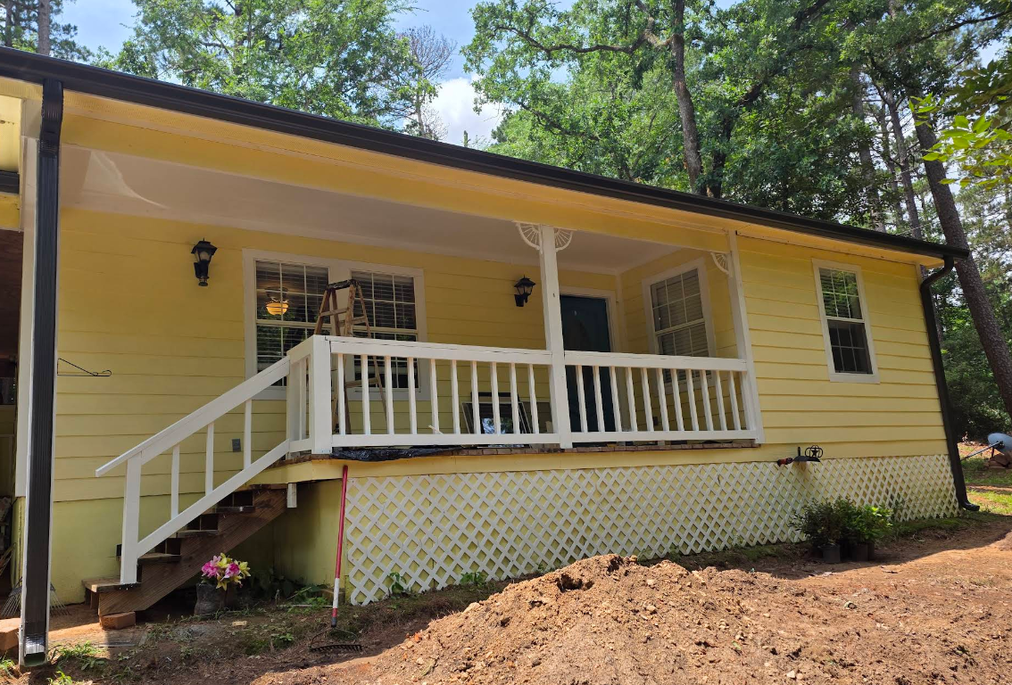 Yellow house with white porch railing and steps, set among trees on a wooded hillside.