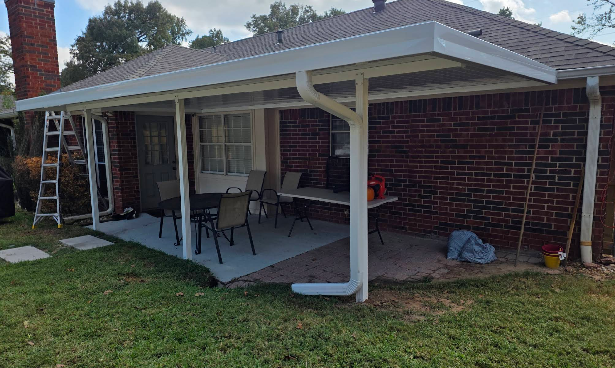 Covered backyard patio with red brick house, white posts, outdoor furniture, and a ladder on the left.