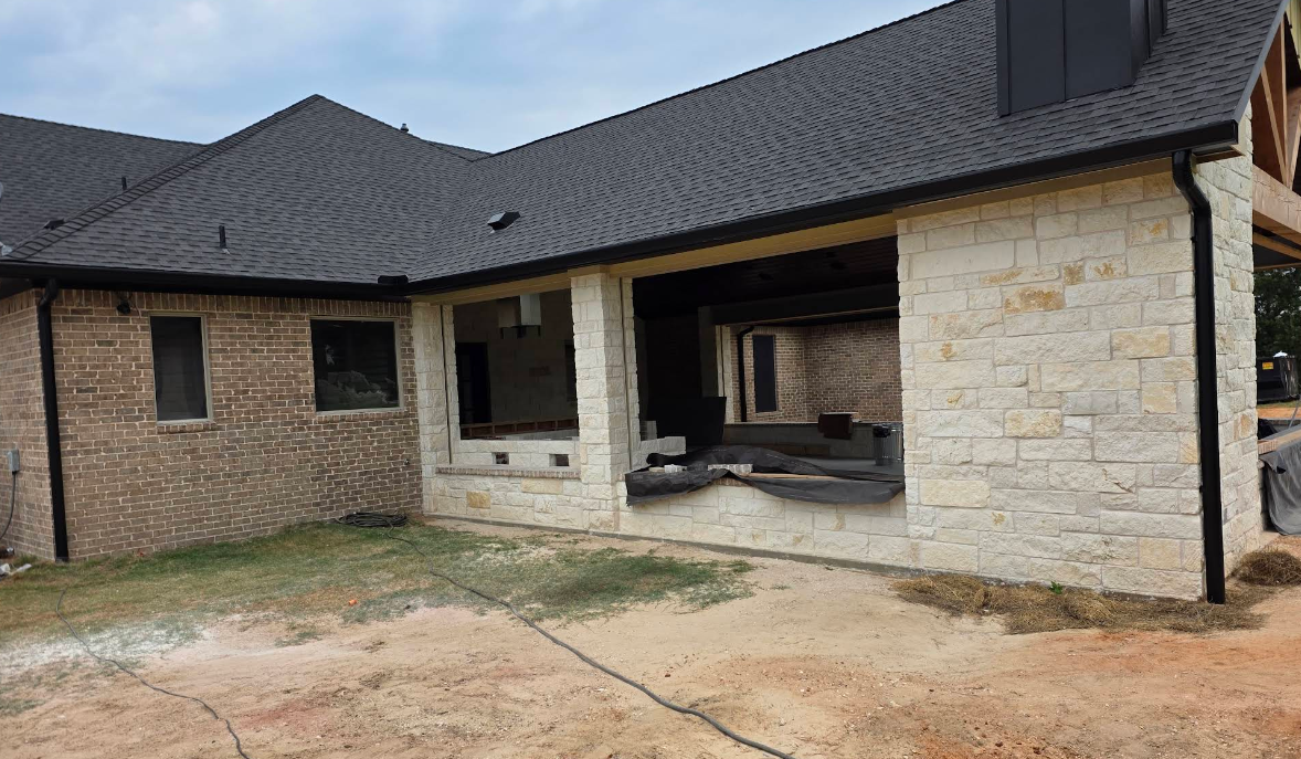 Modern house exterior with dark roof, stone walls, and a covered patio under construction