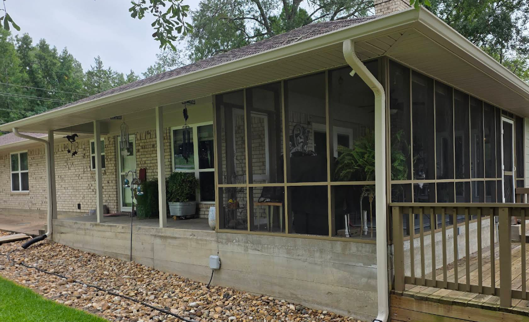 Screened porch on a beige house with a wooden ramp and gravel path, surrounded by trees