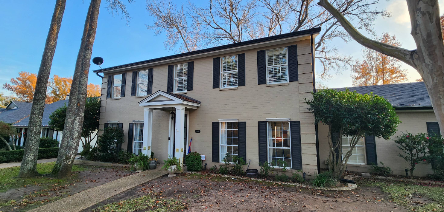 Two-story white house with dark shutters and a front porch, seen from the front yard