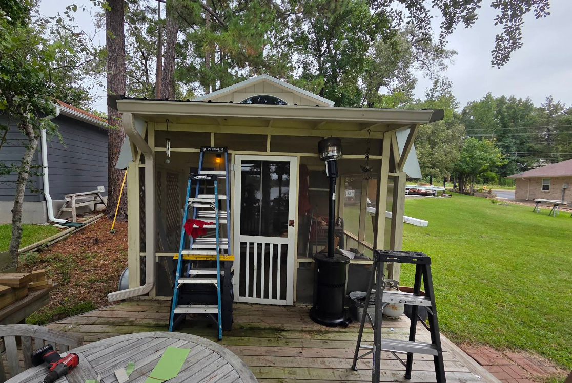 Front porch with a small white house entrance, ladder, and outdoor tools in a grassy yard