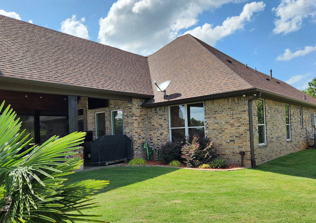 Single-story stone house with brown tiled roof, green lawn, and blue sky with clouds