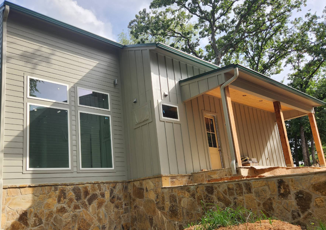 New light gray house with stone foundation and covered front porch under trees