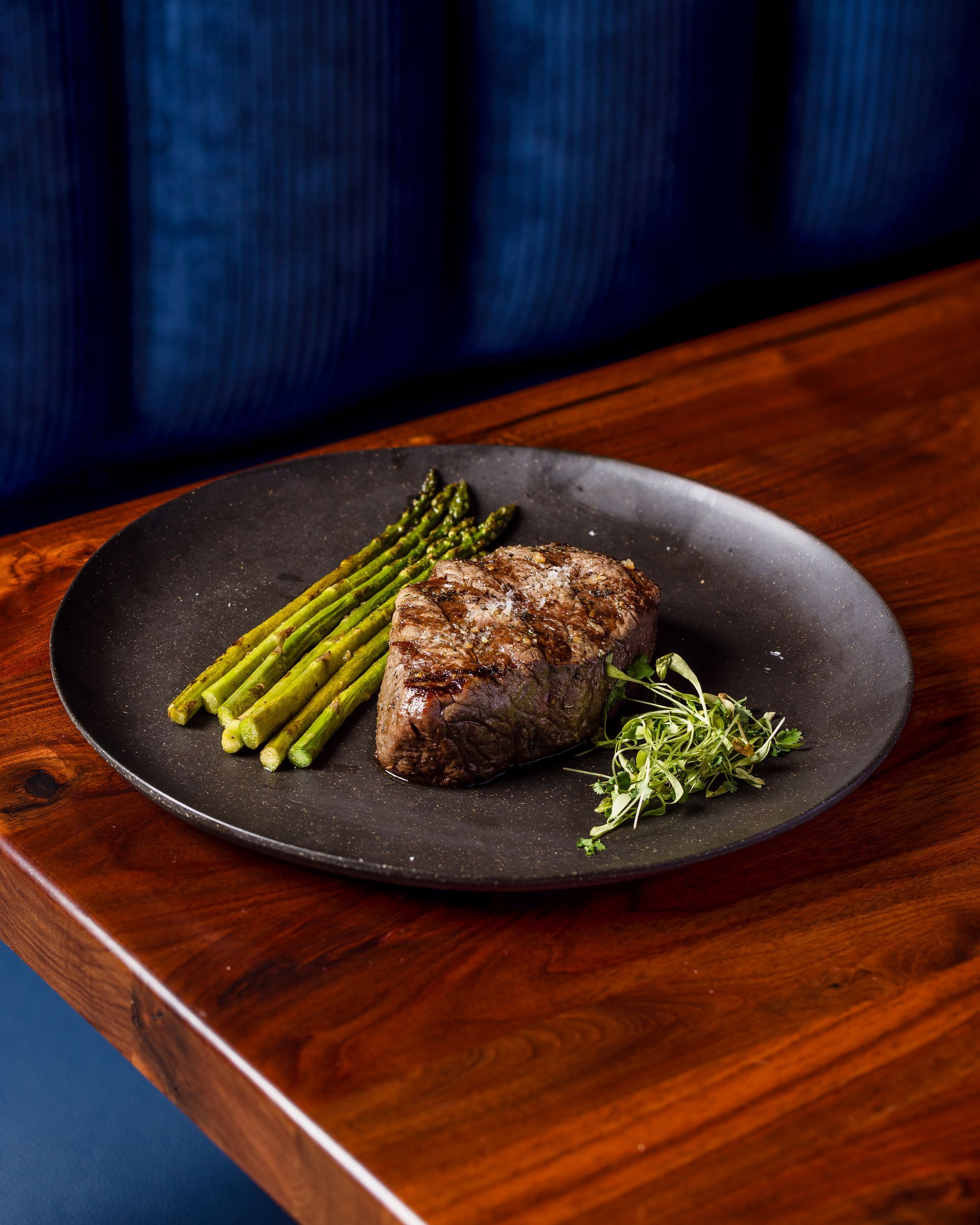 A black plate topped with steak and asparagus on a wooden table