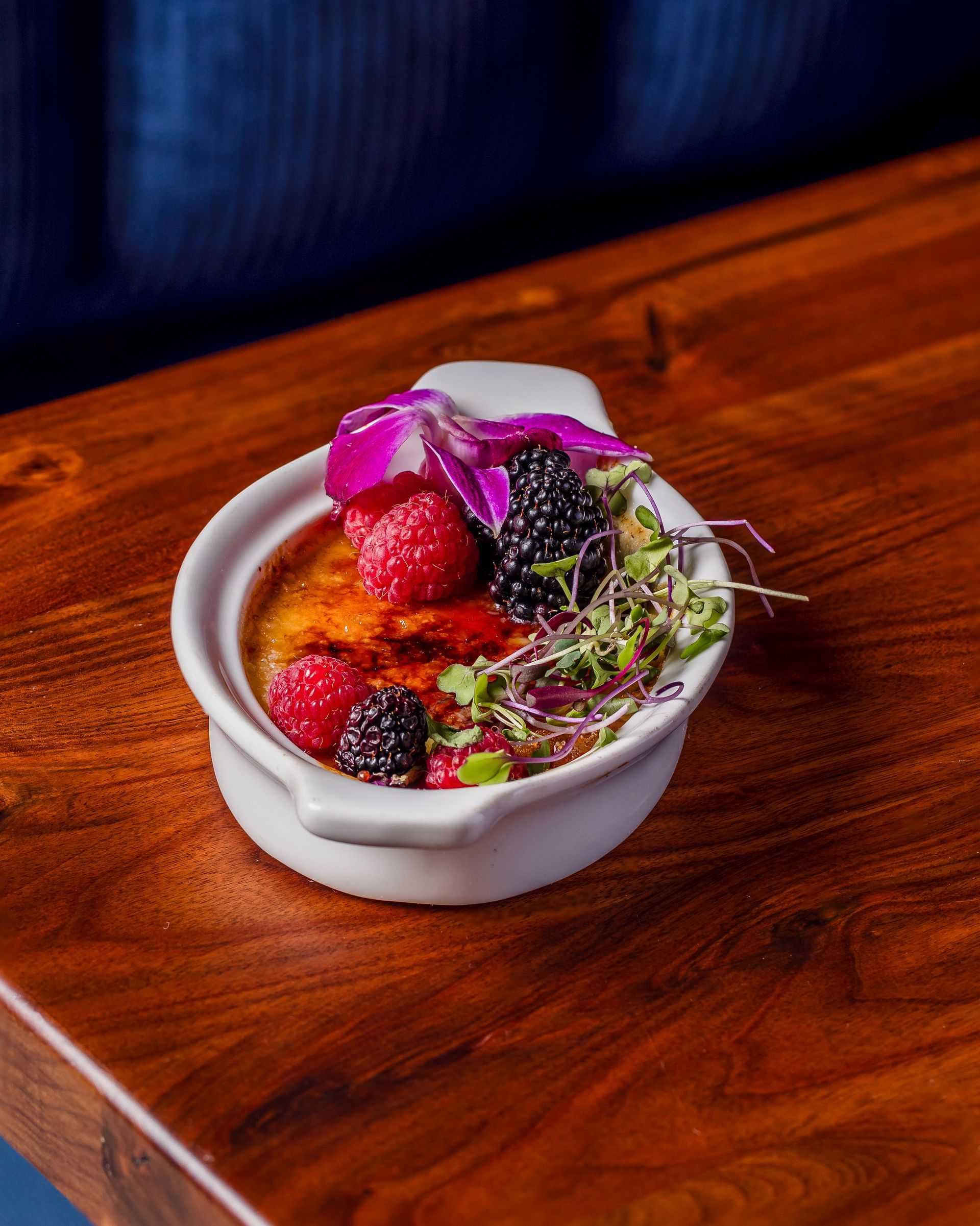 A bowl of food with berries and sprouts on a wooden table.