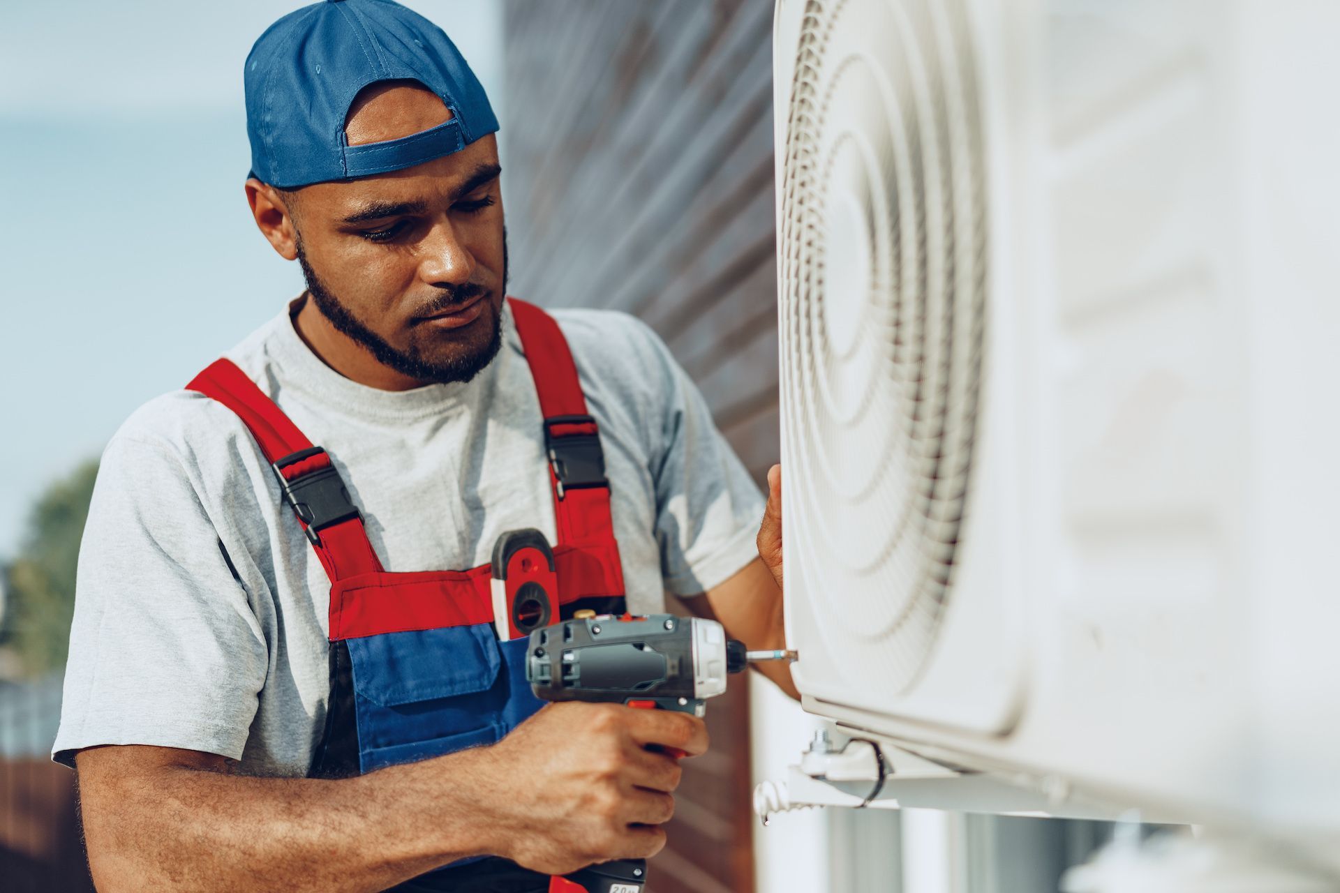 A man is using a drill to fix an air conditioner.