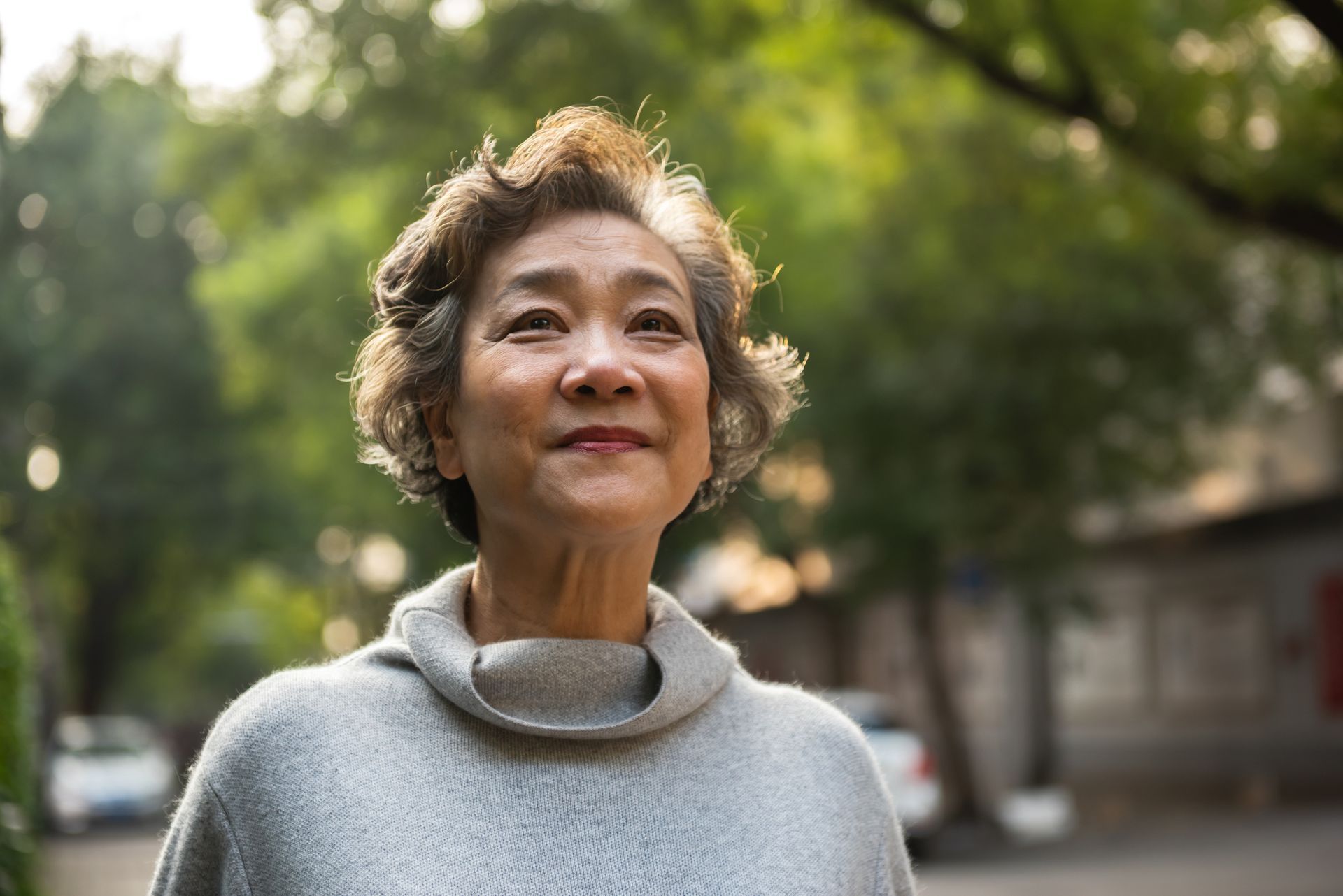 A smiling senior woman enjoys fresh air while sitting peacefully outdoors.