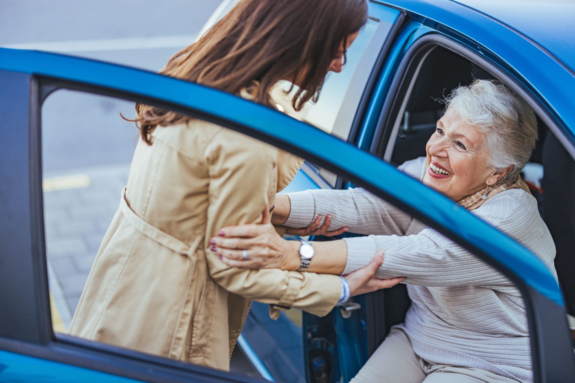 A woman is helping an older woman get out of a car.
