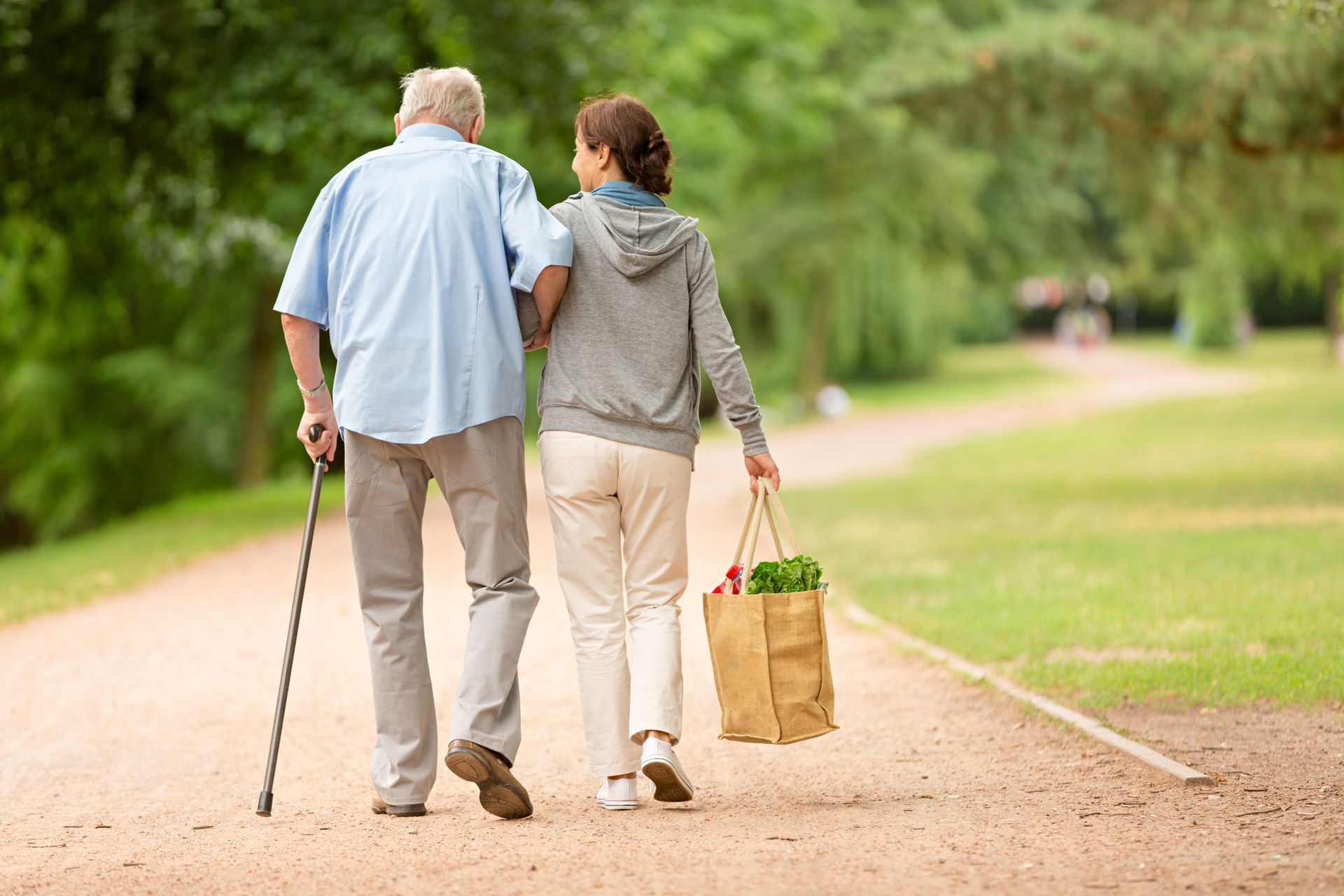 An elderly man and a young woman are walking down a path in a park.
