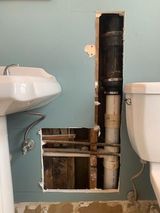 a bathroom with a sink and toilet and a hole in the wall .