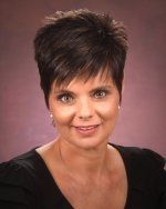 A woman with short hair is wearing a black shirt and smiling for the camera.