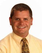 A man in a yellow shirt and tie is smiling for the camera.