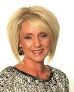 A woman with short blonde hair and earrings is smiling for the camera.