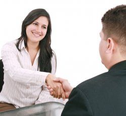 A woman is shaking hands with a man while sitting at a table.