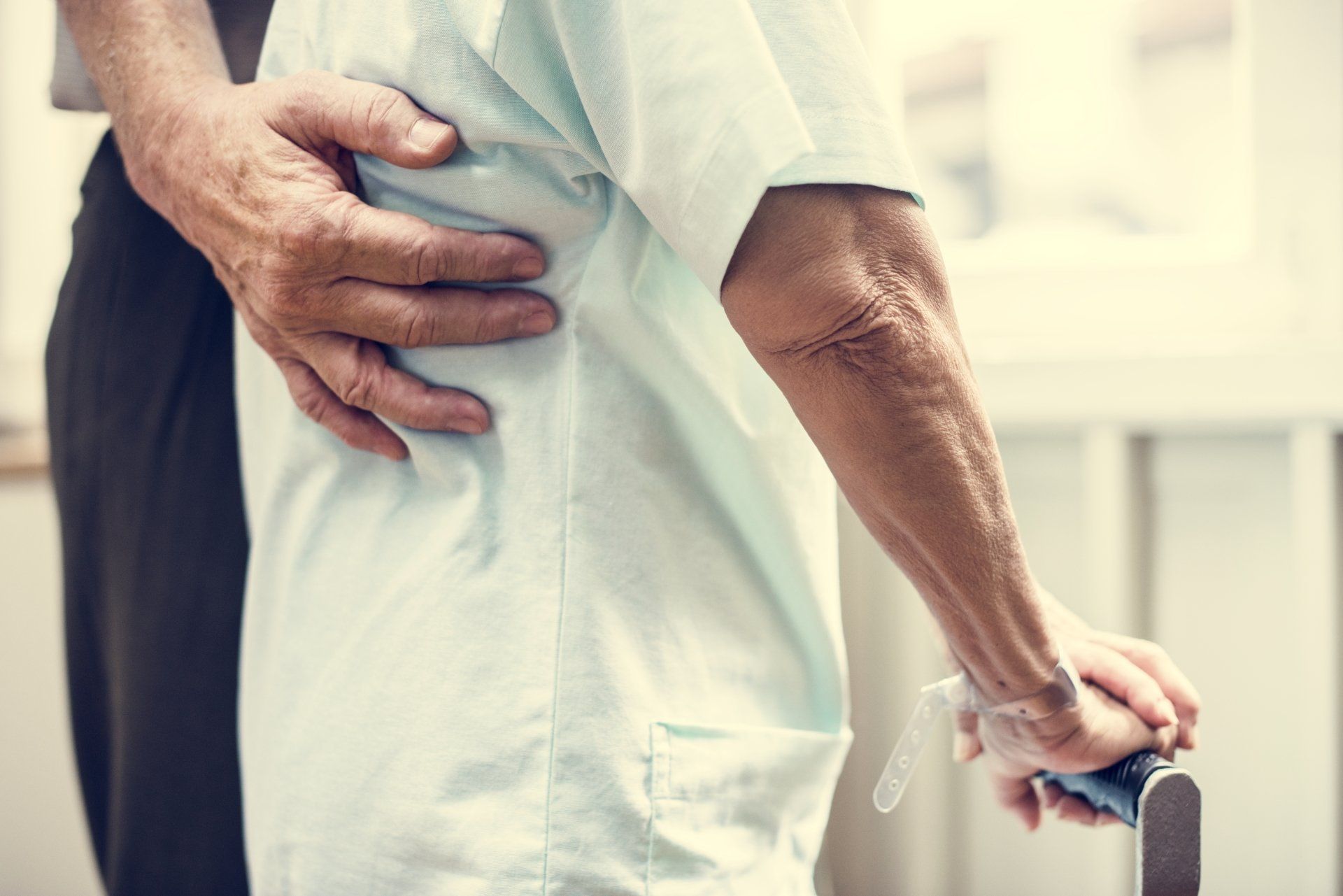 A man is helping an elderly woman walk with a cane.
